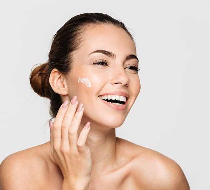 Mujer aplicando crema facial con una sonrisa y piel radiante.